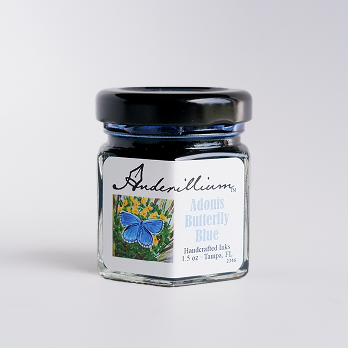 Blue fountain pen ink in a bottle labeled Anderillium Adonis Butterfly Blue, with a close-up of the ink's vibrant color and packaging.