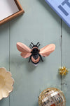 Rose gold paper bumble bee craft by Assembli, shown from a top-down view, featuring intricate details and textured paper design.