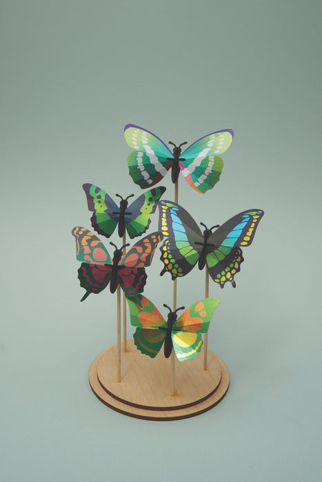Green butterfly DIY craft set by Assembli displayed on a stand, showcasing colorful paper wings and detailed craft components.