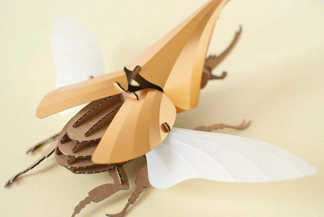 Gold Paper Hercules Beetle craft by Assembli featuring a large, detailed paper beetle with textured gold wings and body.