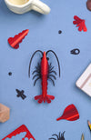 Red paper shrimp craft by Assembli, shown from a top-down view, made of folded paper for creative DIY projects.