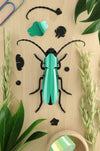 Green Paper Rosalia Beetle craft by Assembli, showcasing detailed, folded paper wings and body on a neutral background.