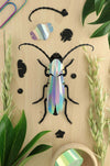 Crafts paper Rosalia beetle by Assembli featuring detailed, colorful paper wings and body on a reflective surface.