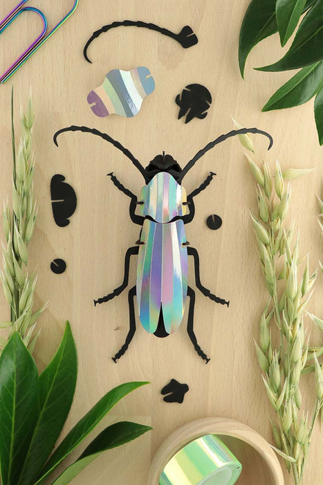 Crafts paper Rosalia beetle by Assembli featuring detailed, colorful paper wings and body on a reflective surface.