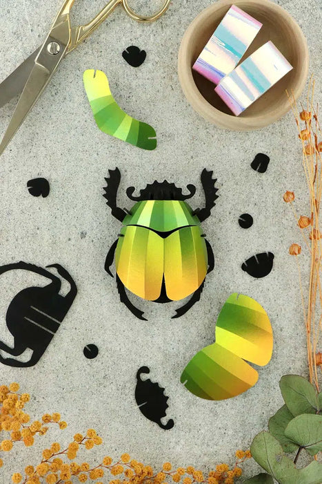 Colorful paper scarab beetle craft by Assembli, showcasing intricate folded paper design in bright mango color.