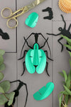 Green paper violin beetle craft by Assembli with intricate folded paper details and vibrant green color.