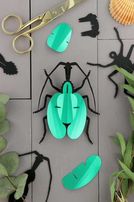 Green paper violin beetle craft by Assembli with intricate folded paper details and vibrant green color.