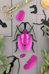 Pink paper craft violin beetle made by Assembli, showing detailed folded paper wings and body on a plain background.