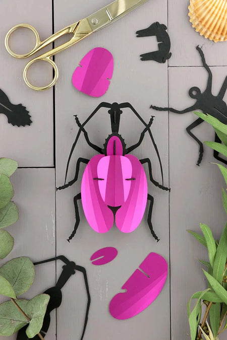 Pink paper craft violin beetle made by Assembli, showing detailed folded paper wings and body on a plain background.