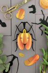 Yellow paper violin craft by Assembli, showcasing a detailed handmade paper model of a violin beetle.