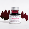 Papier Plume burgundy fountain pen ink bottle with ink flowing into a glass jar, showcasing rich burgundy color and elegant design.