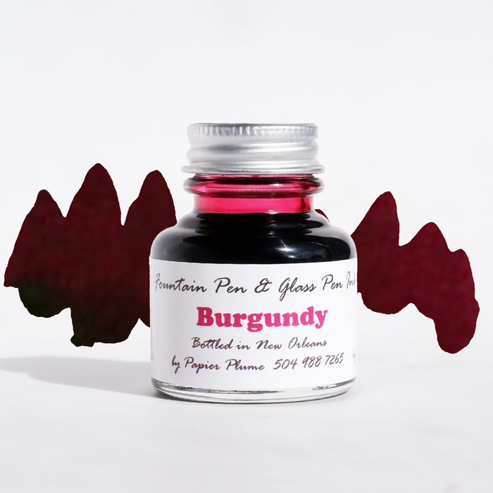 Papier Plume burgundy fountain pen ink bottle with ink flowing into a glass jar, showcasing rich burgundy color and elegant design.
