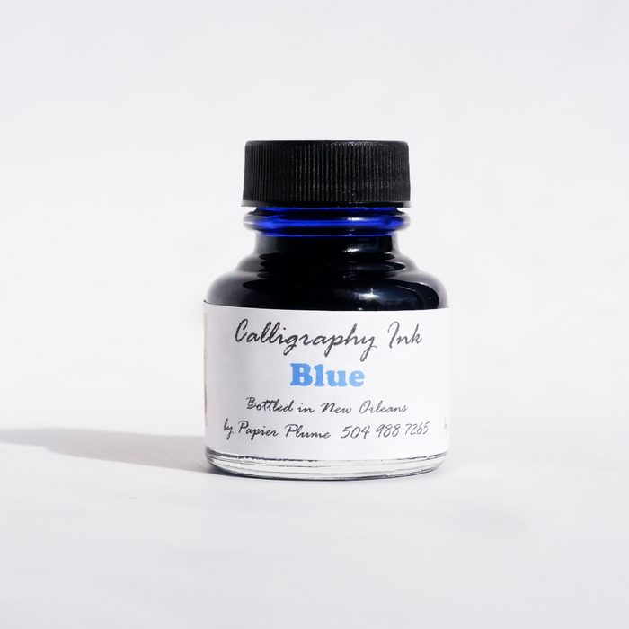 Blue Papier Plume bottled calligraphy ink in a clear glass bottle with a black screw cap, showcasing smooth, vibrant ink.