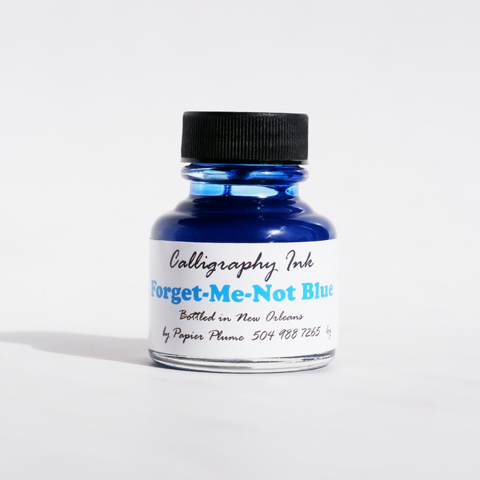 Bottle of Papier Plume calligraphy ink in Forget-Me-Not Blue with a clear glass container and blue ink inside.