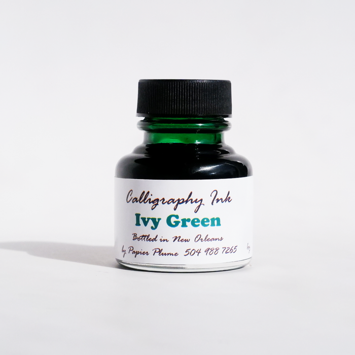 Papier Plume bottled calligraphy ink in vibrant ivy green, with a glass ink bottle and calligraphy pen on a white background.