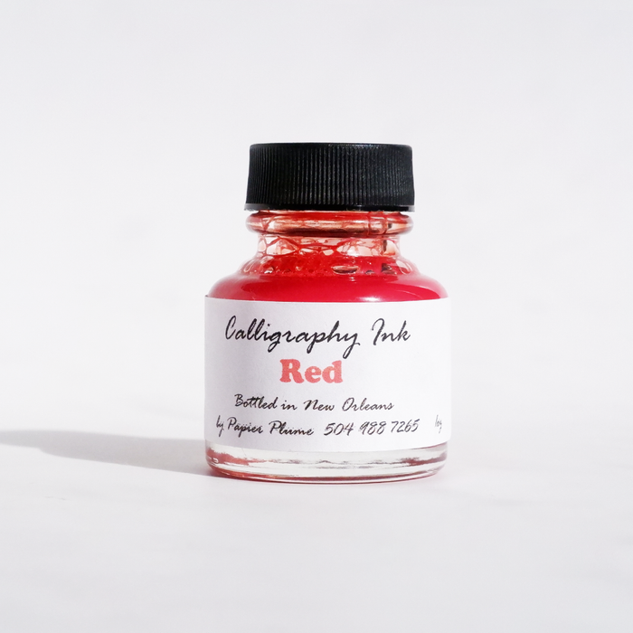 Red bottled calligraphy ink from Papier Plume, showcasing vibrant ink in a clear glass bottle with a black screw cap.