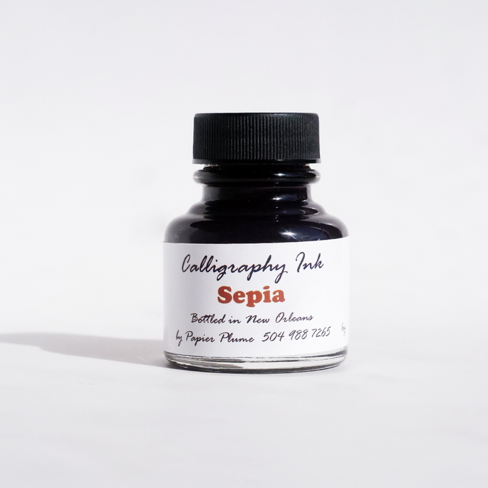 Papier Plume bottled calligraphy ink in sepia, showing a glass ink bottle with a black cap and a calligraphy pen.