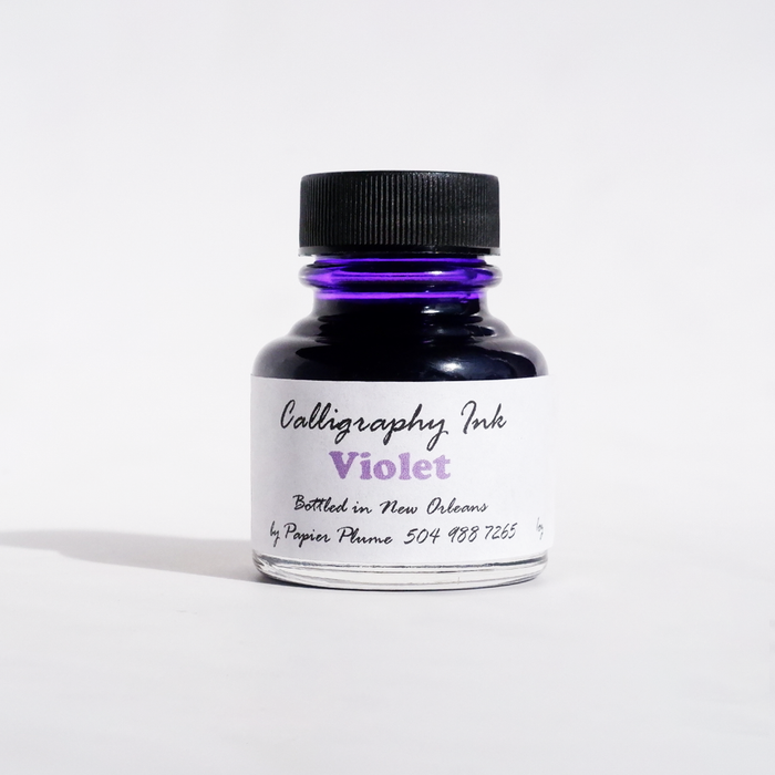 Violet bottled calligraphy ink by Papier Plume in a glass container with a black screw cap, designed for artistic writing.