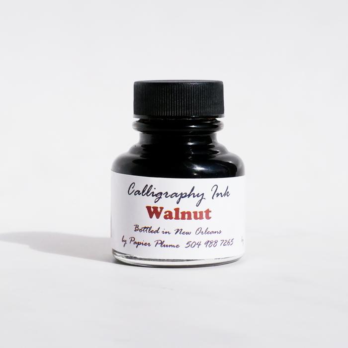 Bottle of Papier Plume Walnut Calligraphy Ink showing the dark brown ink inside a clear glass bottle.