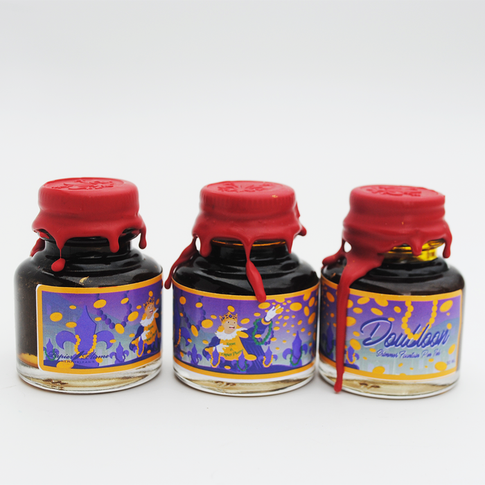 Papier Plume Doubloon shimmer fountain pen ink in a glass bottle with gold accents, showcasing the vibrant ink color.