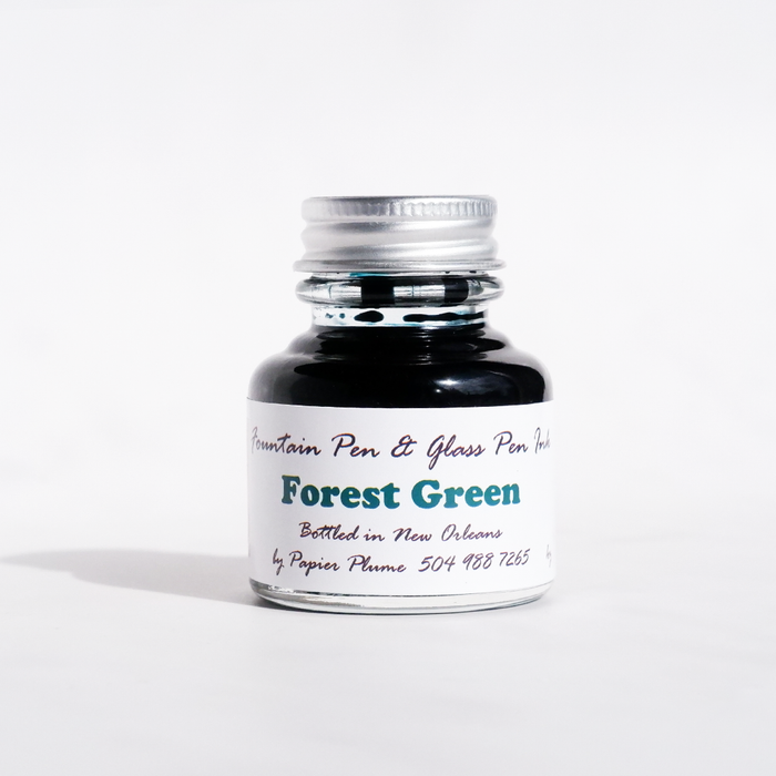 Papier Plume forest green fountain pen ink in a glass bottle, vibrant green ink visible through the transparent container.
