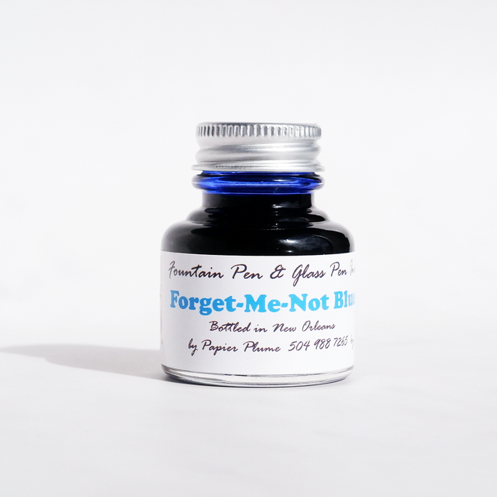 Papier Plume Forget-Me-Not Blue fountain pen ink bottle with vibrant blue ink visible in the glass container.