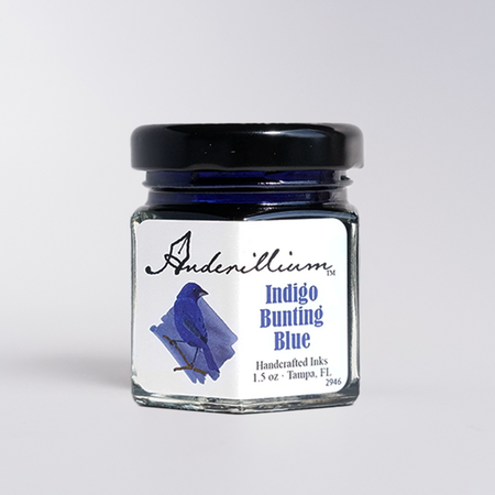 Anderillium Indigo Bunting Blue fountain pen ink in a glass bottle with colorful label, showcasing vibrant blue ink.