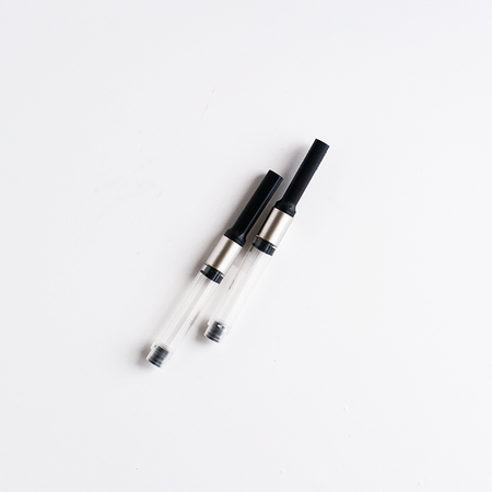 Lamy Z27 converter for ink cartridges, shown in close-up with transparent plastic body and metal twist mechanism.