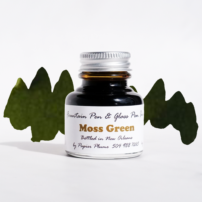 Moss green Papier Plume fountain pen ink bottle with ink flowing into a glass ink well on a white background.