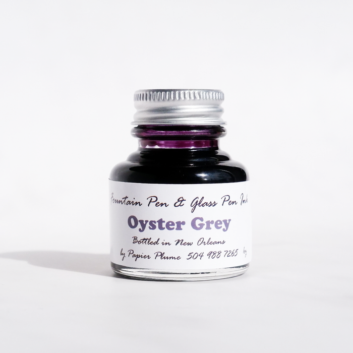 Bottle of Papier Plume fountain pen ink in oyster grey color, with a clear glass container and ink label visible.