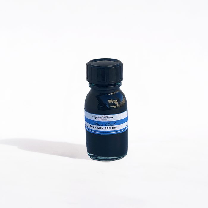 Papier Plume Pavo Real fountain pen ink in a glass bottle with vibrant blue and green ink inside.
