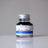 Papier Plume Pavo Real fountain pen ink in a glass bottle with vibrant blue and green ink visible inside.