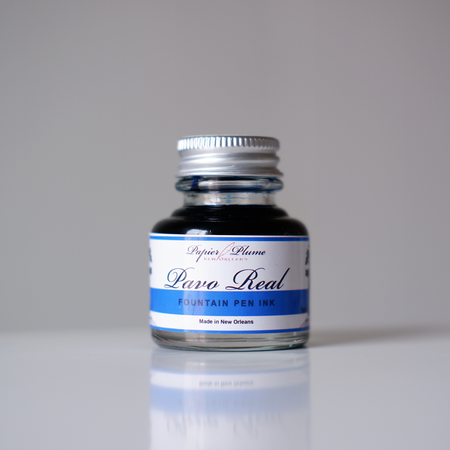 Papier Plume Pavo Real fountain pen ink in a glass bottle with vibrant blue and green ink visible inside.