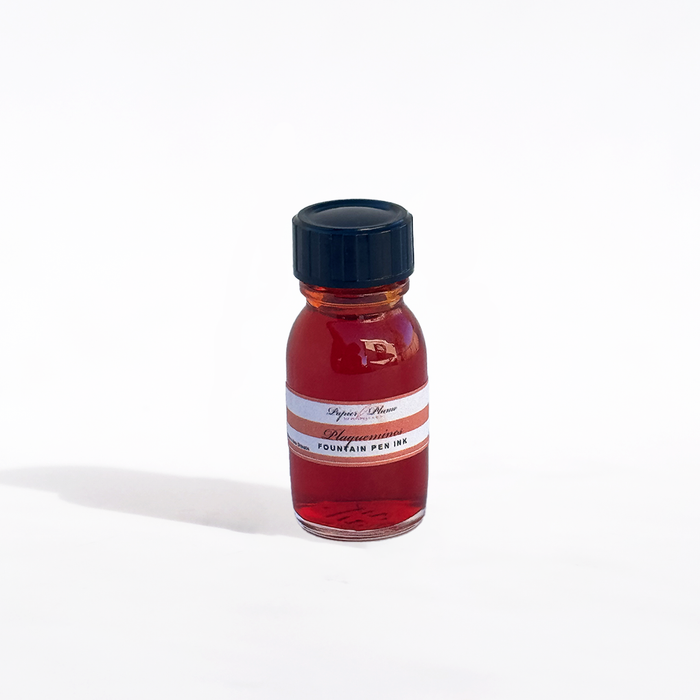 Papier Plume Plaquemines fountain pen ink bottle with deep red liquid in a glass container on a white background.