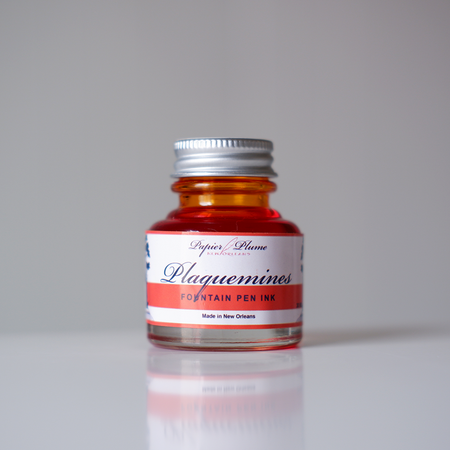 Close-up of Papier Plume Plaquemines fountain pen ink bottle with vibrant ink inside, showcasing the elegant ink packaging and branding.