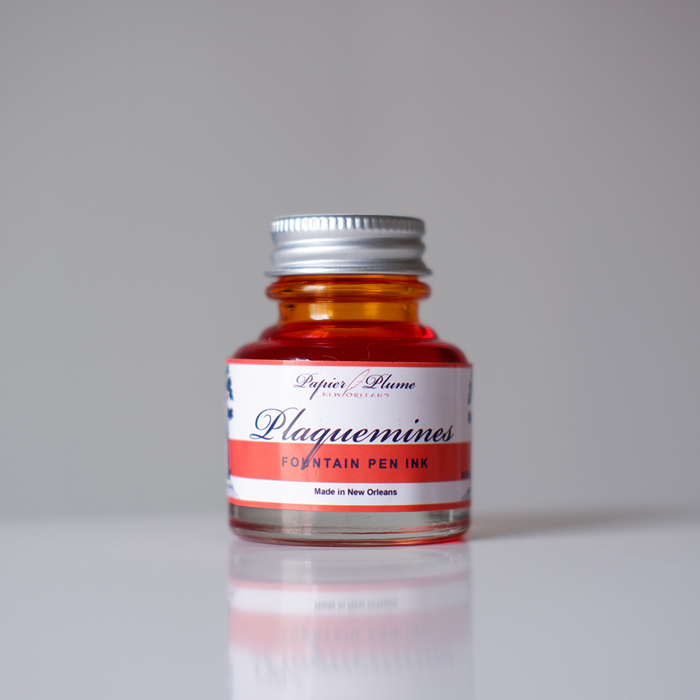 Close-up of Papier Plume Plaquemines fountain pen ink bottle with vibrant ink inside, showcasing the elegant ink packaging and branding.