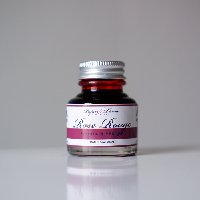 Papier Plume Rose Rouge fountain pen ink bottle with red ink inside, showcasing its vibrant color and elegant packaging.
