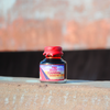 Papier Plume Rusty Rainbow shimmer fountain pen ink bottle with vibrant, multi-colored ink visible in the glass container.