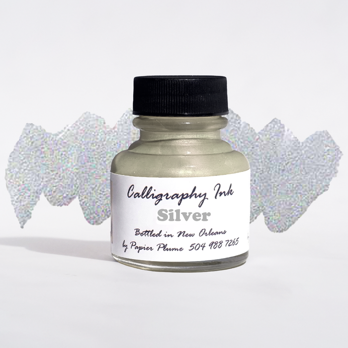 Bottled metallic silver calligraphy ink from Papier Plume, showcasing the shiny ink inside a clear glass bottle with a black cap.