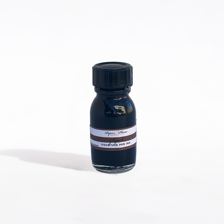 Papier Plume fountain pen ink in a Sapele wood-inspired bottle with rich amber-colored ink visible inside.