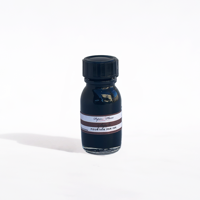 Papier Plume fountain pen ink in a Sapele wood-inspired bottle with rich amber-colored ink visible inside.