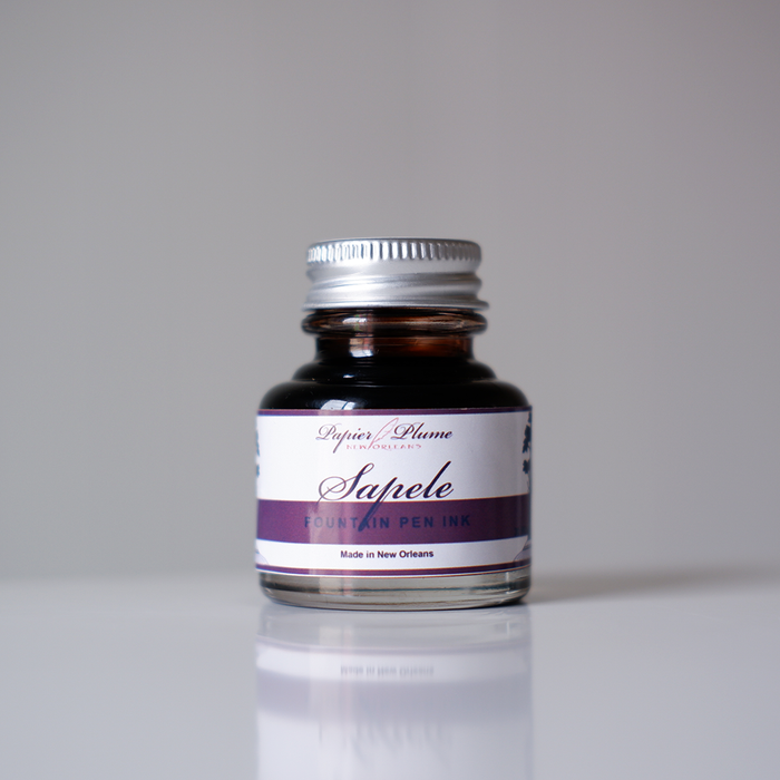 Bottle of Papier Plume Sapele Fountain Pen Ink showing the dark amber liquid in a glass container.