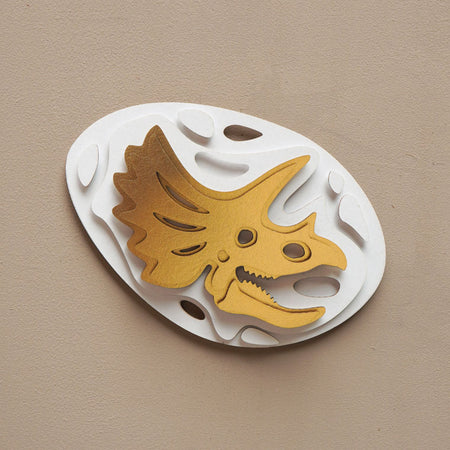 Gold paper fossil art of a Triceratops by Assembli, featuring detailed fossil-inspired design on a neutral background.