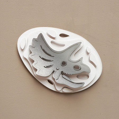 Silver paper fossil art of a Triceratops by Assembli, showcasing detailed prehistoric dinosaur design on textured paper.