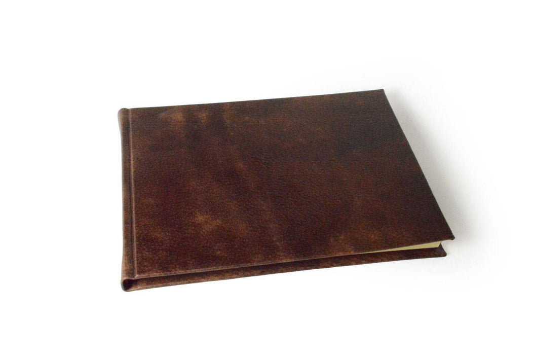 Large handcrafted guest book with marbleized cover and leather trim by Il Cartiglio, featuring blank pages for guests to sign.