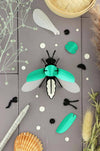 Emerald green metallic Paper Firefly craft by Assembli, made from shimmering paper with detailed wings and body.