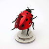 Colorful paper ladybug and lovebug craft by Assembli, featuring vibrant red and black paper bugs with decorative details.
