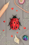 Colorful paper ladybug and lovebug craft by Assembli, featuring vibrant red and black wings with detailed paper wings and body.