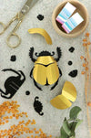 Colorful rainbow paper scarab beetle craft made from folded paper by Assembli, showcasing vibrant, intricate origami-style design.
