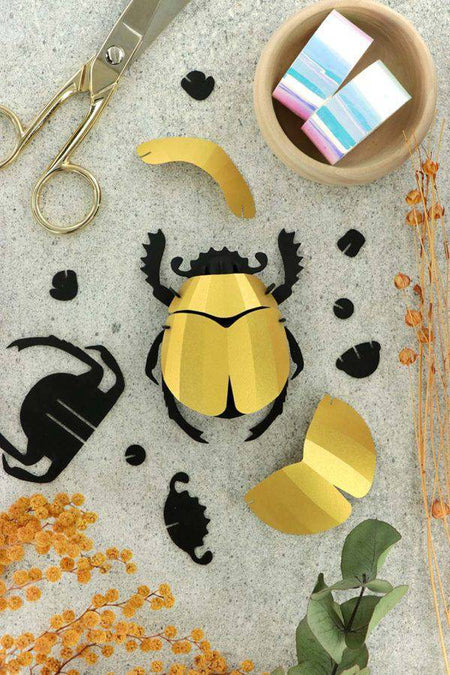 Colorful rainbow paper scarab beetle craft made from folded paper by Assembli, showcasing vibrant, intricate origami-style design.